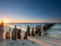 Zachód słońca nad Bałtykiem, idealne miejsce na wakacje w Polsce nad morzem. Drewniane pale na plaży tworzą malowniczy krajobraz.
