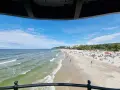 Słoneczna plaża z tłumem turystów, gdzie jest najcieplejsze morze. Woda faluje, a na piasku rozłożone są parawany i ręczniki.