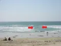 Dwie czerwone strzałki wskazują na prąd morski w Bałtyku, gdzie widać ludzi na plaży i w wodzie.