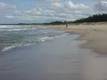 Plaża z falującym morzem i osobą w czerwonej bluzie na piasku.