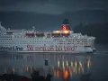 Duży biały prom Stena Line z czerwonym napisem "Bli med og bli blid!" płynie po wodzie o zmierzchu.