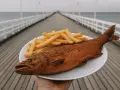 Talerz z smażoną rybą i frytkami na tle molo i morza.