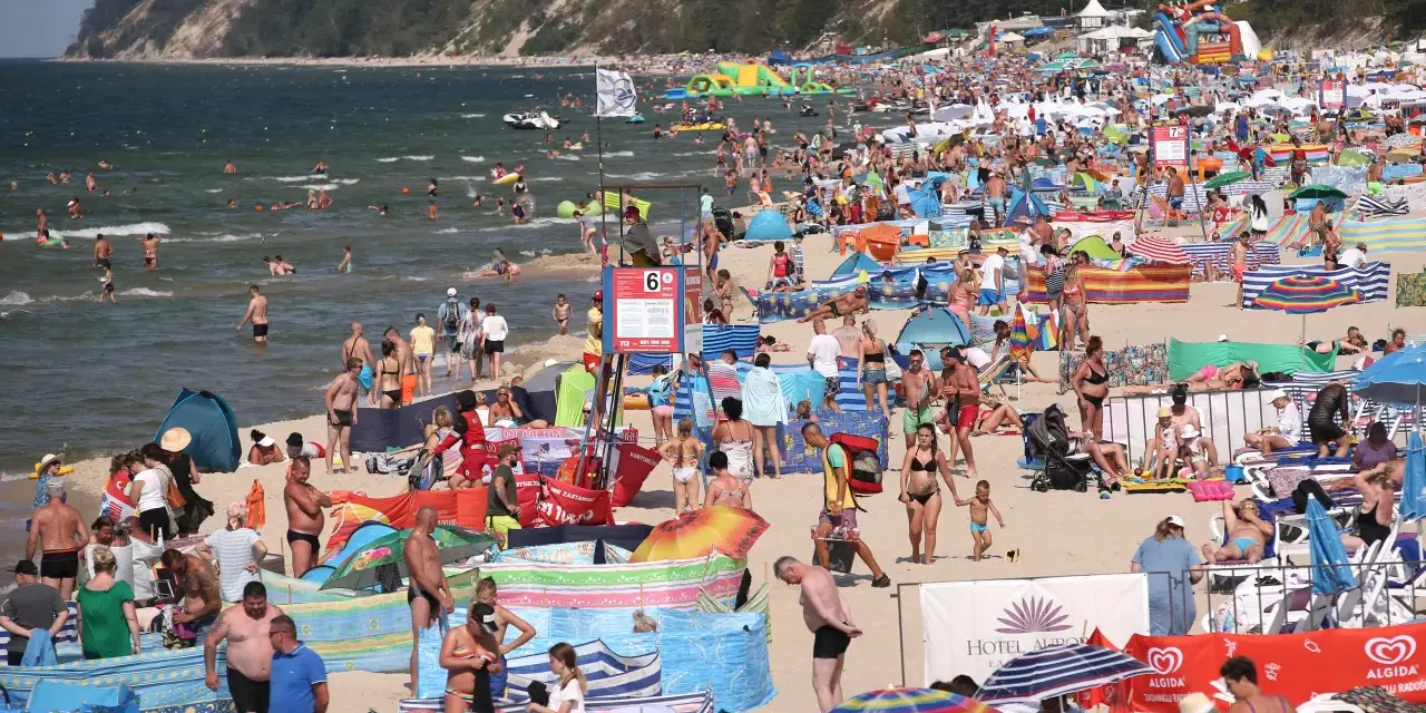 Tłum ludzi na plaży, w wodzie i na piasku. Wiele kolorowych parawanów i parasoli. W tle klif porośnięty lasem. Czy Morze Czarne jest ciepłe? Tłumy sugerują, że tak!