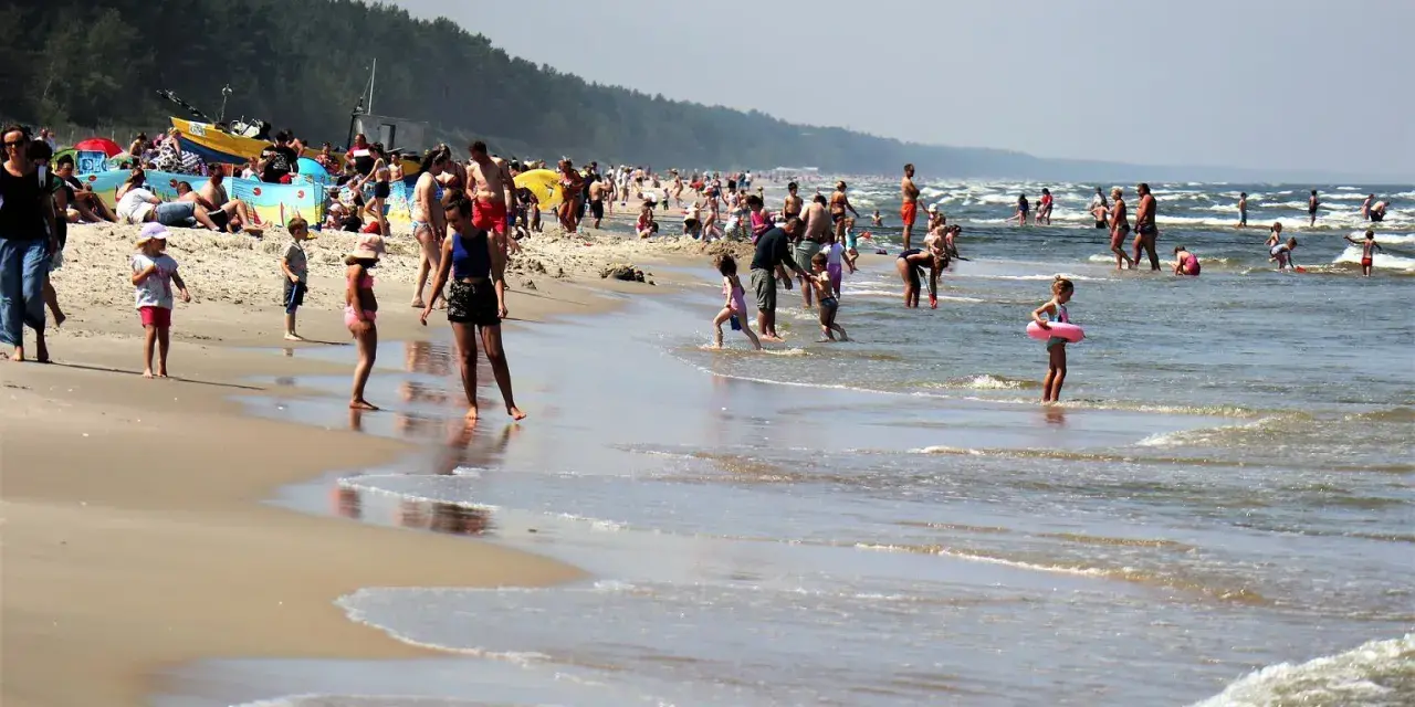 Ludzie kąpią się w Bałtyku, szukając miejsca, gdzie jest najcieplejsza woda. Słoneczny dzień na plaży z rodzinami i dziećmi.