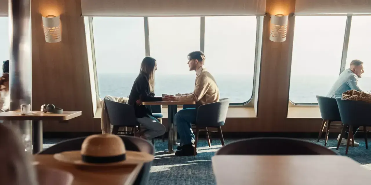 Para zakochanych trzyma się za ręce przy oknie na statku Stena Line. Romantyczne chwile i atrakcje na morzu.