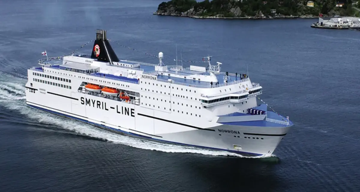 Duży biały prom "Smyril-Line Norrona" płynie po spokojnym morzu, w tle widać zielone wybrzeże.