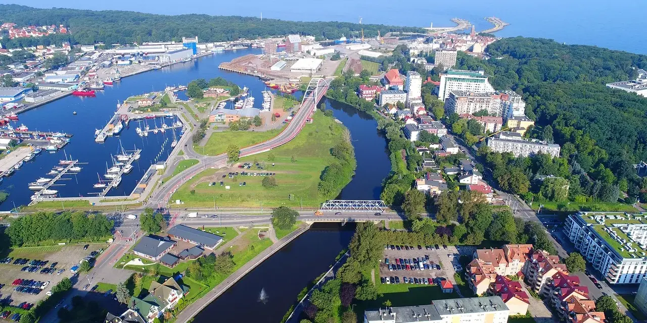 Widok z lotu ptaka na port i miasto. Warto zobaczyć w Kołobrzegu: marinę z jachtami, mosty nad rzeką, zabudowę miejską i zieleń.