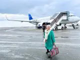 Kobieta z kolorową torbą na lotnisku, gotowa do podróży. Samolot Atlantic Airways z napisem "Faroe Islands" sugeruje, jak dostać się na Wyspy Owcze.