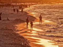 Zachód słońca na plaży, ludzie spacerują, fale delikatnie obmywają brzeg. Ciekawe, ile stopni ma Bałtyk w taką pogodę?