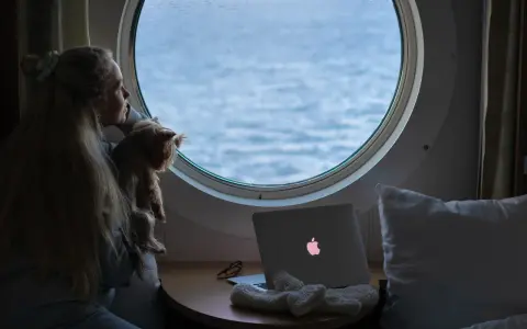 Dziewczyna z psem patrzy przez okrągłe okno na morze. Obok leży laptop z podświetlonym logo, jak prom nova star.