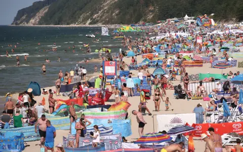 Tłum ludzi na plaży, w wodzie i na piasku. Wiele kolorowych parawanów i parasoli. W tle klif porośnięty lasem. Czy Morze Czarne jest ciepłe? Tłumy sugerują, że tak!