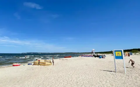 Słoneczna plaża Cztery Wiatry z piaskiem, morzem i ludźmi. W oddali widać ratownika na wieży.