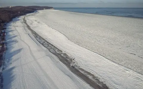 Zamarznięta plaża i Bałtyk, jakby czas się zatrzymał od kiedy powstało morze bałtyckie. W oddali widać statki.