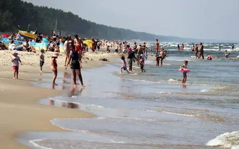 Ludzie kąpią się w Bałtyku, szukając miejsca, gdzie jest najcieplejsza woda. Słoneczny dzień na plaży z rodzinami i dziećmi.