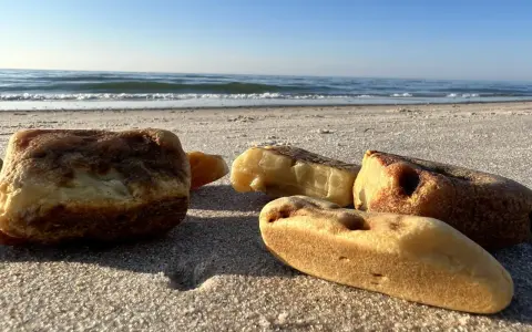 Kawałki bursztynu na piaszczystej plaży, z widokiem na spokojne morze i błękitne niebo.