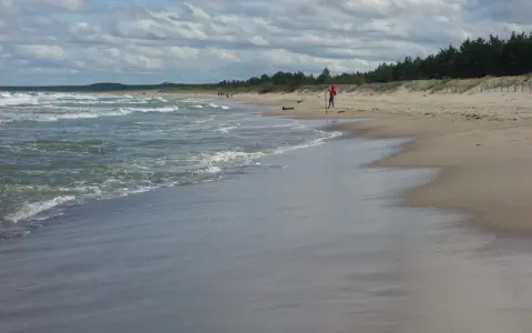 Plaża z falującym morzem i osobą w czerwonej bluzie na piasku.