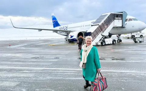 Kobieta z kolorową torbą na lotnisku, gotowa do podróży. Samolot Atlantic Airways z napisem "Faroe Islands" sugeruje, jak dostać się na Wyspy Owcze.