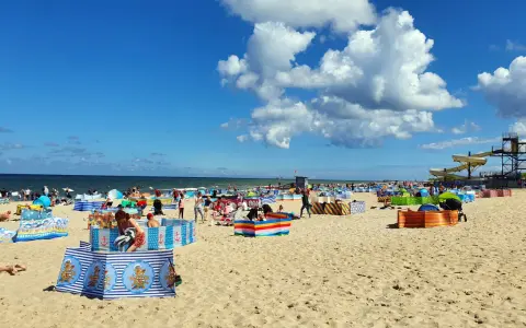 Władysławowo z dzieckiem: plaża pełna kolorowych parawanów, ludzi odpoczywających i bawiących się na piasku, w tle morze i zjeżdżalnie wodne.