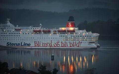 Duży biały prom Stena Line z czerwonym napisem "Bli med og bli blid!" płynie po wodzie o zmierzchu.