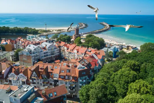 Piękna, słoneczna pogoda w Kołobrzegu. Widok na miasto, port i plażę, mewy szybujące nad Bałtykiem.