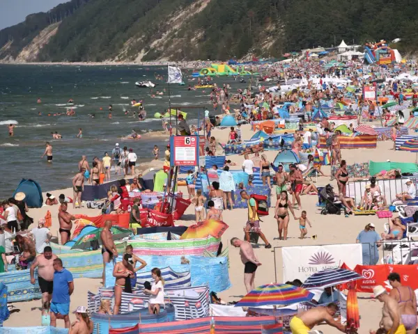 Tłum ludzi na plaży, w wodzie i na piasku. Wiele kolorowych parawanów i parasoli. W tle klif porośnięty lasem. Czy Morze Czarne jest ciepłe? Tłumy sugerują, że tak!