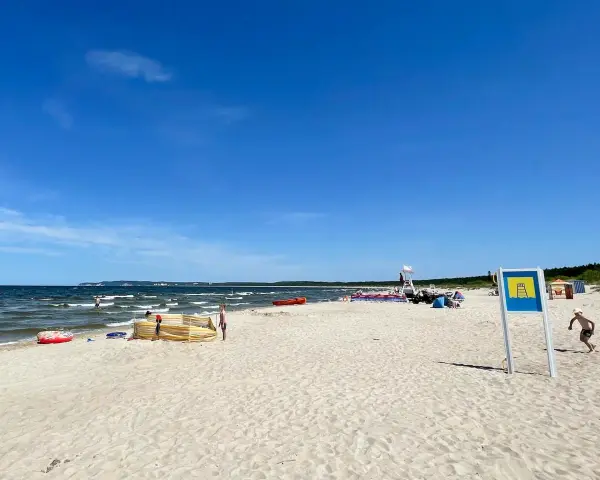Słoneczna plaża Cztery Wiatry z piaskiem, morzem i ludźmi. W oddali widać ratownika na wieży.