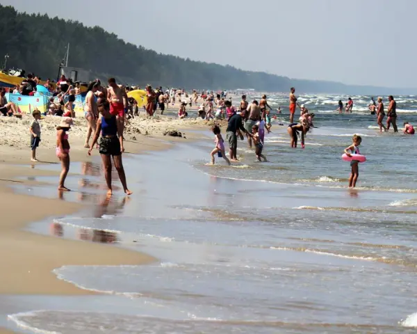 Ludzie kąpią się w Bałtyku, szukając miejsca, gdzie jest najcieplejsza woda. Słoneczny dzień na plaży z rodzinami i dziećmi.