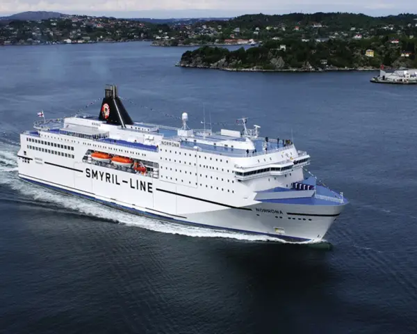 Duży biały prom "Smyril-Line Norrona" płynie po spokojnym morzu, w tle widać zielone wybrzeże.