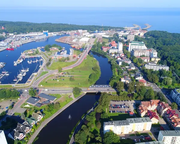 Widok z lotu ptaka na port i miasto. Warto zobaczyć w Kołobrzegu: marinę z jachtami, mosty nad rzeką, zabudowę miejską i zieleń.