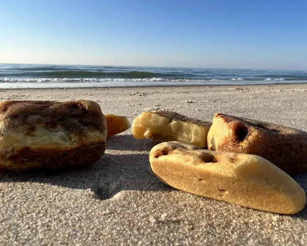 Kawałki bursztynu na piaszczystej plaży, z widokiem na spokojne morze i błękitne niebo.
