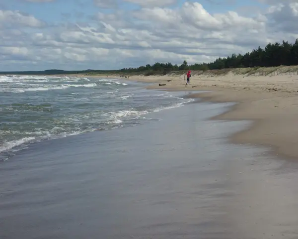 Plaża z falującym morzem i osobą w czerwonej bluzie na piasku.