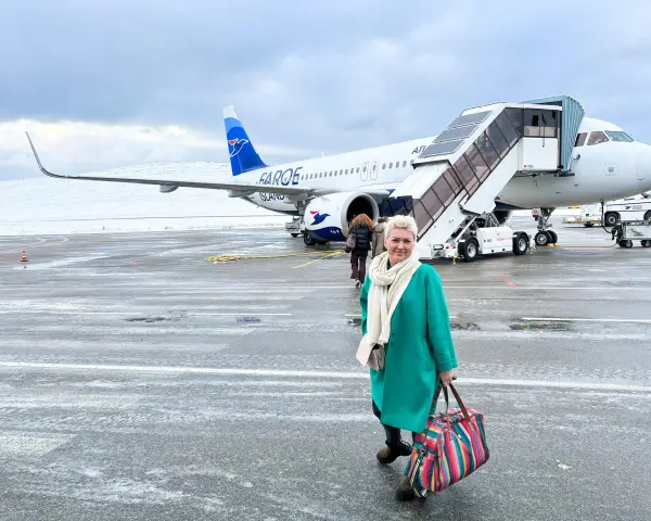 Kobieta z kolorową torbą na lotnisku, gotowa do podróży. Samolot Atlantic Airways z napisem "Faroe Islands" sugeruje, jak dostać się na Wyspy Owcze.