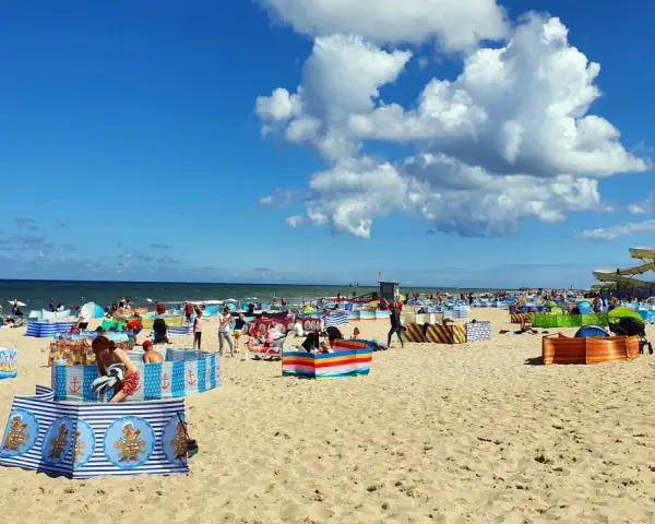 Władysławowo z dzieckiem: plaża pełna kolorowych parawanów, ludzi odpoczywających i bawiących się na piasku, w tle morze i zjeżdżalnie wodne.