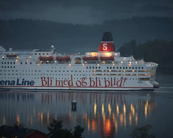 Duży biały prom Stena Line z czerwonym napisem "Bli med og bli blid!" płynie po wodzie o zmierzchu.