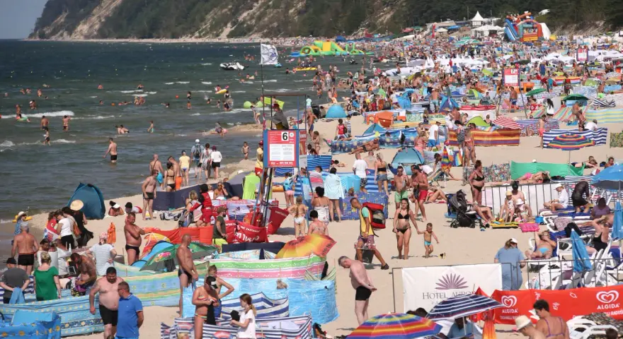 Tłum ludzi na plaży, w wodzie i na piasku. Wiele kolorowych parawanów i parasoli. W tle klif porośnięty lasem. Czy Morze Czarne jest ciepłe? Tłumy sugerują, że tak!