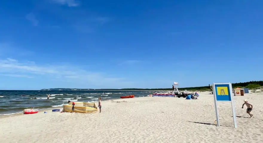 Słoneczna plaża Cztery Wiatry z piaskiem, morzem i ludźmi. W oddali widać ratownika na wieży.