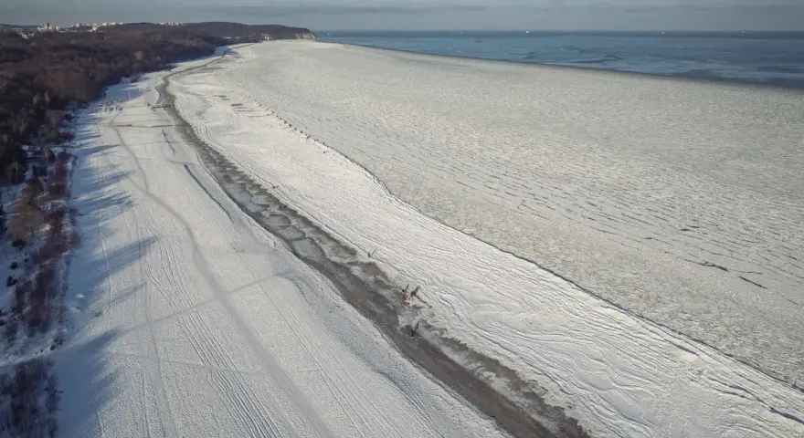Zamarznięta plaża i Bałtyk, jakby czas się zatrzymał od kiedy powstało morze bałtyckie. W oddali widać statki.