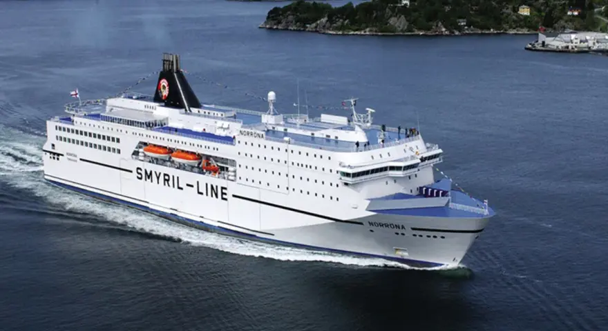 Duży biały prom "Smyril-Line Norrona" płynie po spokojnym morzu, w tle widać zielone wybrzeże.