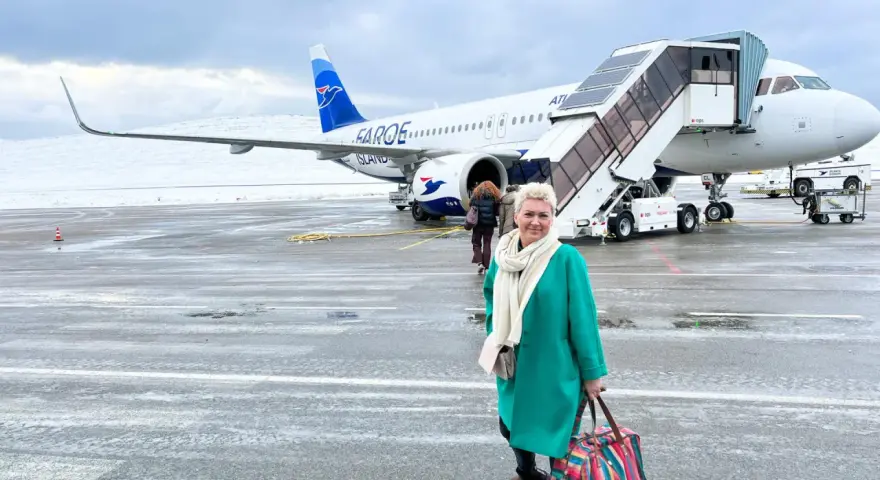 Kobieta z kolorową torbą na lotnisku, gotowa do podróży. Samolot Atlantic Airways z napisem "Faroe Islands" sugeruje, jak dostać się na Wyspy Owcze.