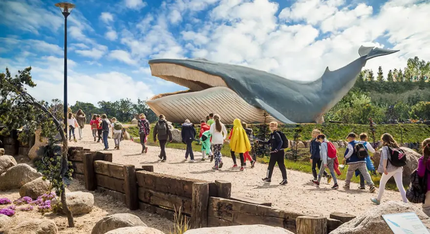 Grupa dzieci zwiedza park z gigantycznym modelem wieloryba. Władysławowo atrakcje dla dzieci oferują niezapomniane wrażenia.