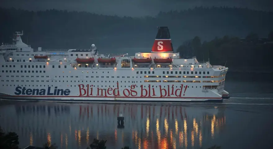 Duży biały prom Stena Line z czerwonym napisem "Bli med og bli blid!" płynie po wodzie o zmierzchu.