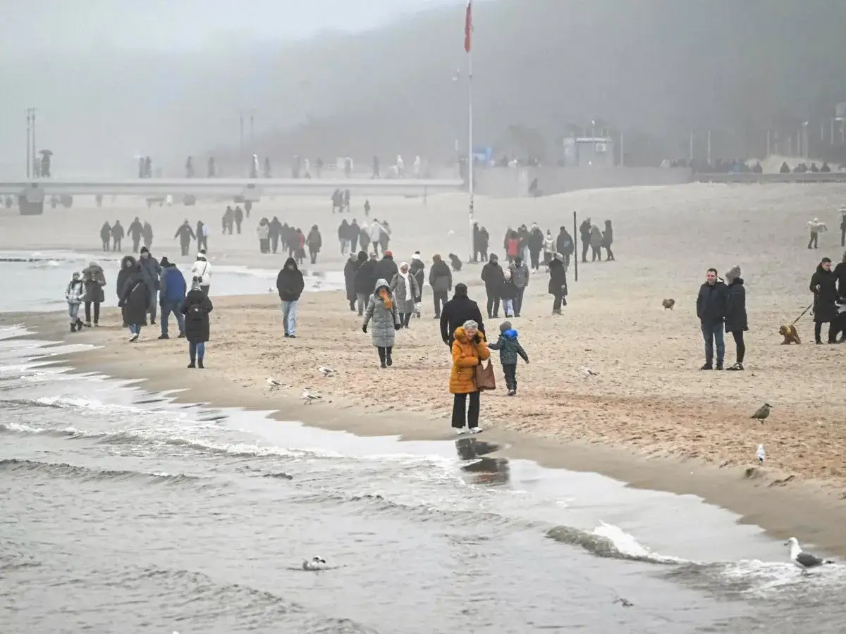 Ludzie spacerują po plaży, kiedy sztormy na Bałtyku tworzą mglistą, ponurą atmosferę. Fale delikatnie rozbijają się o brzeg.
