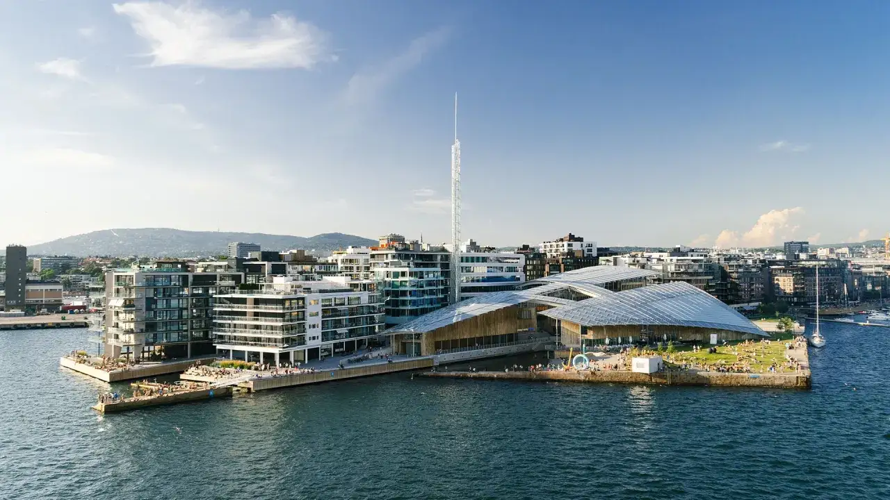 Nowoczesna architektura nad wodą w Oslo. Warto zobaczyć to miejsce, gdzie ludzie odpoczywają na trawie i przy nabrzeżu.