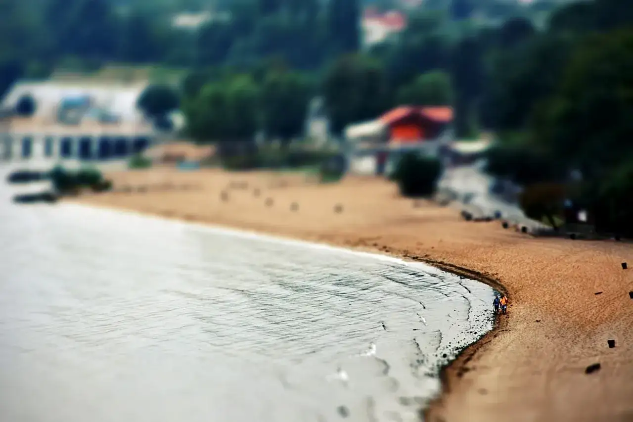 Plaża w Dąbkach, z dwoma spacerującymi ludźmi. Warto tam jechać na wypoczynek.