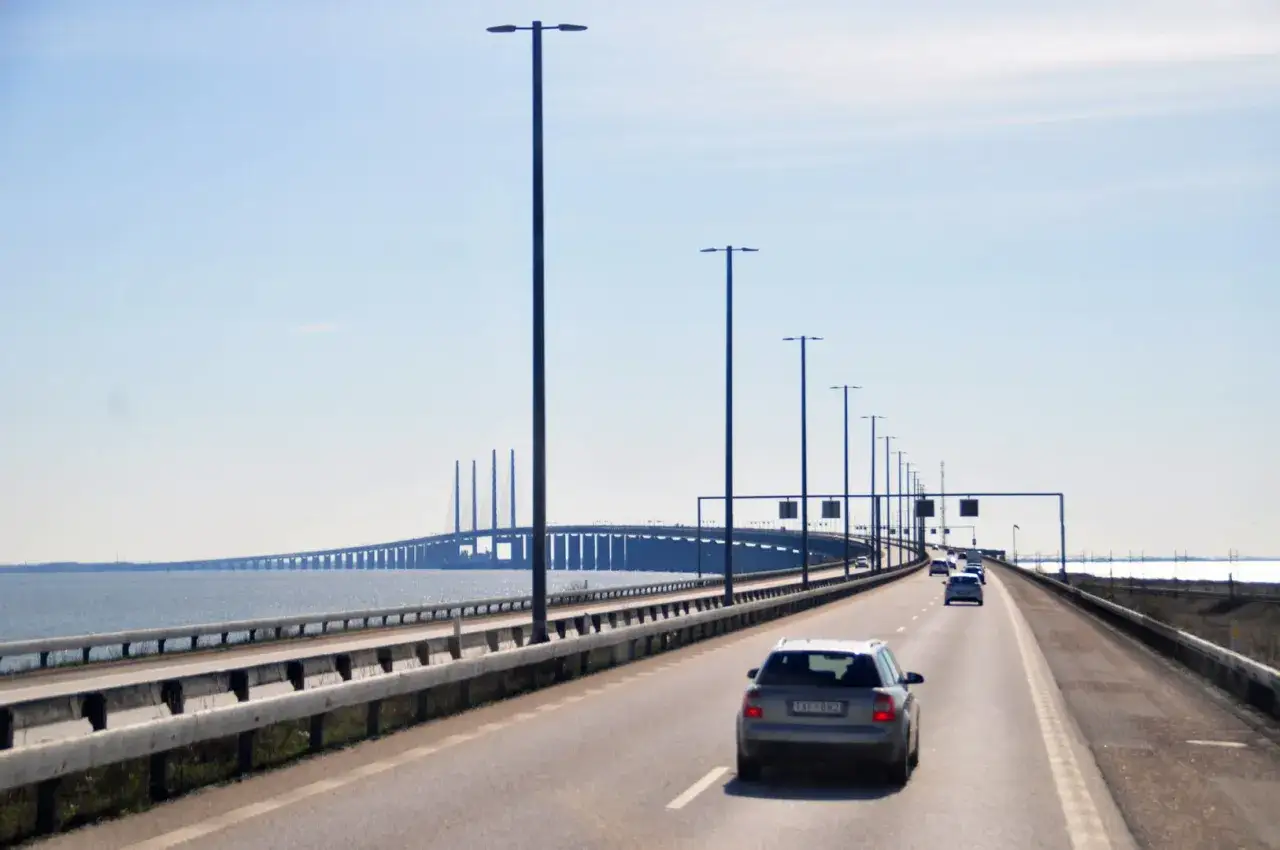Droga na imponującym moście łączącym Kopenhagę z Malmö. Samochody jadą w kierunku widocznego w oddali, charakterystycznego mostu.