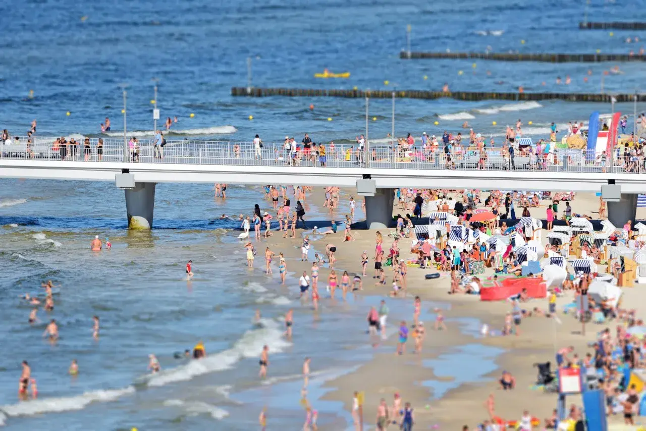 Tłum ludzi na plaży i molo, woda w Bałtyku jest płytka i ciepła, idealna do kąpieli.