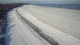 Zamarznięta plaża i Bałtyk, jakby czas się zatrzymał od kiedy powstało morze bałtyckie. W oddali widać statki.