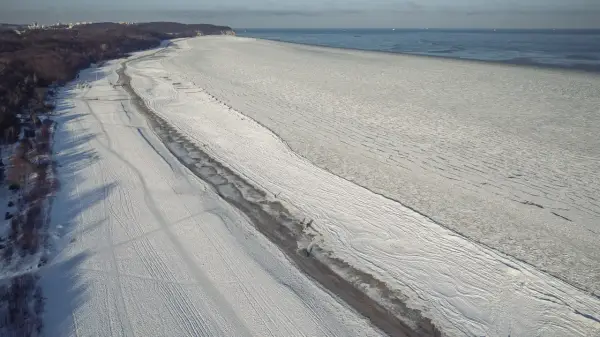 Zamarznięta plaża i Bałtyk, jakby czas się zatrzymał od kiedy powstało morze bałtyckie. W oddali widać statki.