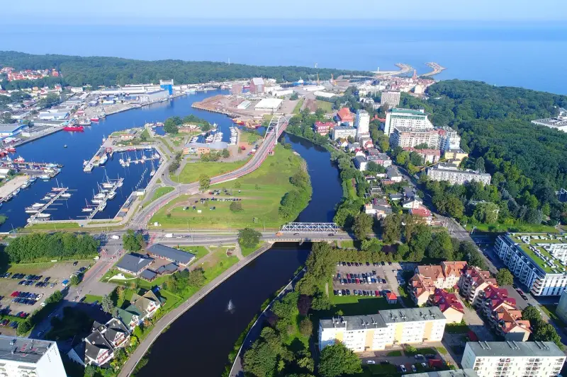 Widok z lotu ptaka na port i miasto. Warto zobaczyć w Kołobrzegu: marinę z jachtami, mosty nad rzeką, zabudowę miejską i zieleń.